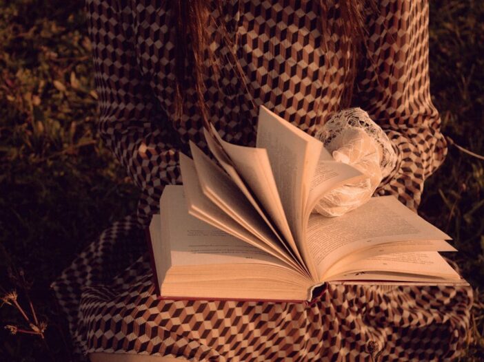 Close-up of a woman in a patterned dress reading an open book outdoors — inspiring book quotes about life and literature