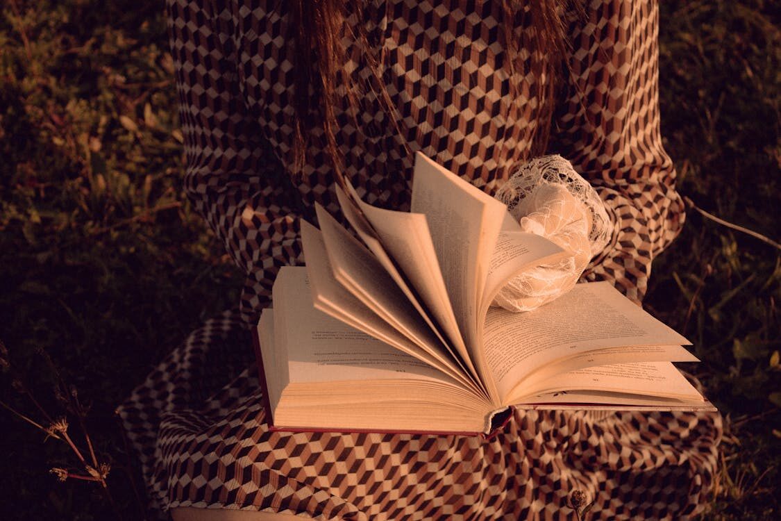 Close-up of a woman in a patterned dress reading an open book outdoors — inspiring book quotes about life and literature