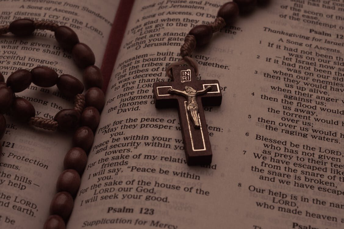 Wooden rosary and crucifix resting on open Bible pages showing Psalms, symbolizing prayer, healing, and spiritual reflection.