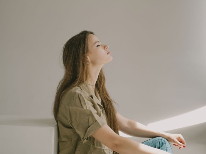 Side profile of a young woman sitting indoors, lost in thought with eyes closed.