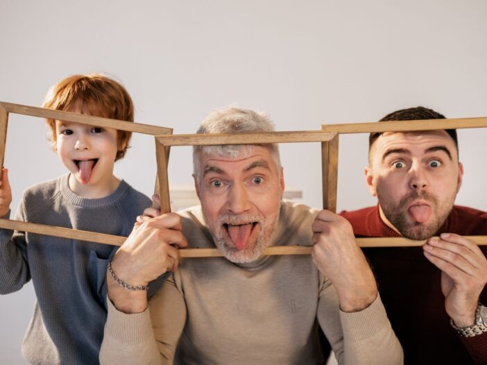 Grandfather, father, and son making funny faces indoors with wooden frames.