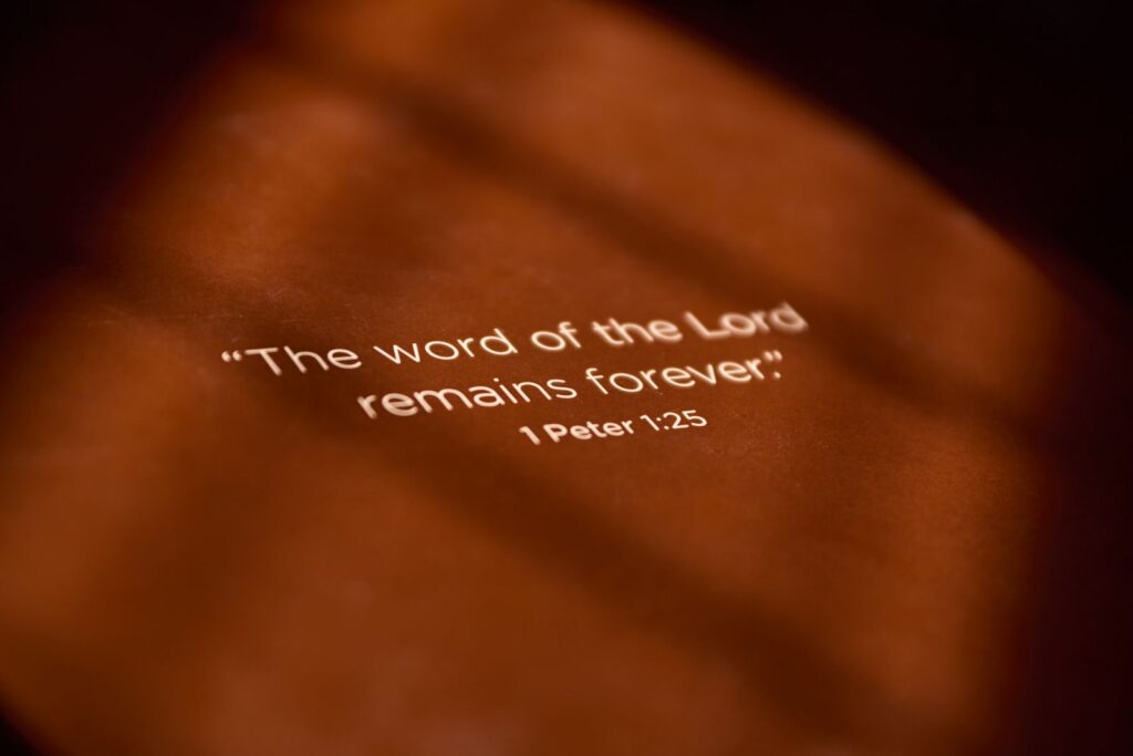 Inspirational Bible verse from 1 Peter 1:25 on a textured orange surface.