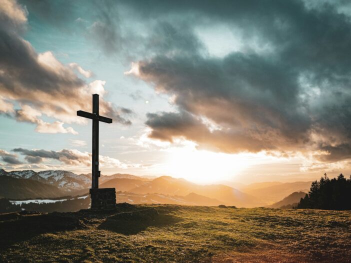 a cross sitting on top of a lush green hillside