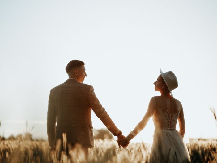 A newlywed couple holding hands in a sunlit field, llustrating the meaning of “love is patient, love is kind” in marriage.