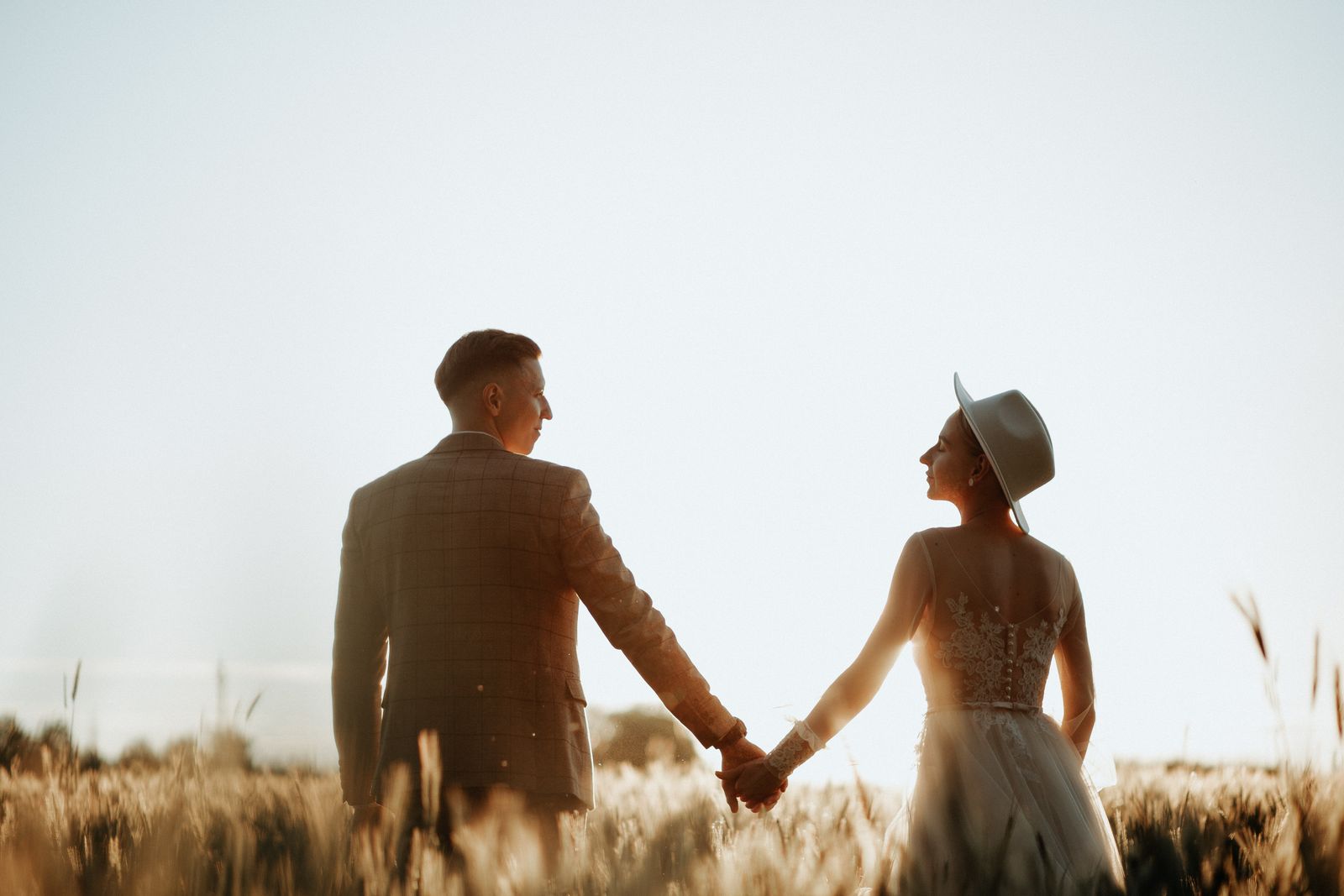 A newlywed couple holding hands in a sunlit field, llustrating the meaning of “love is patient, love is kind” in marriage.