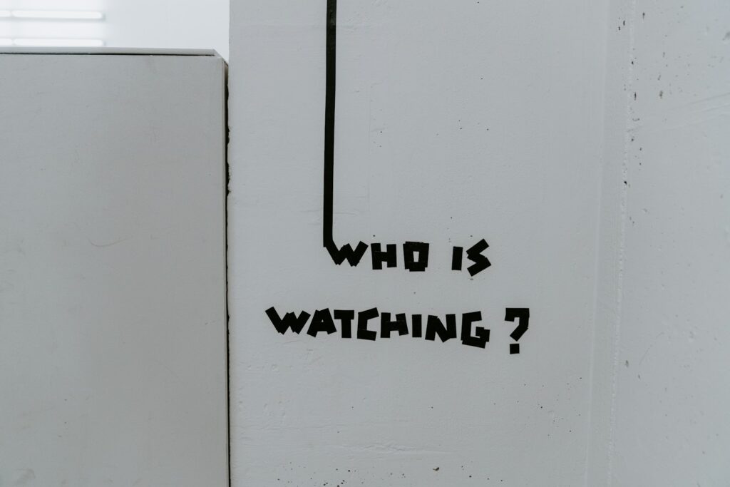Graffiti reading “Who is watching?” on a wall, representing surveillance and the “Big Brother is watching you” theme in George Orwell’s 1984.