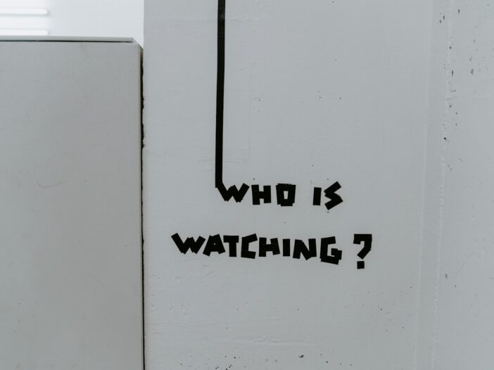 Graffiti reading “Who is watching?” on a wall, representing surveillance and the “Big Brother is watching you” theme in George Orwell’s 1984.