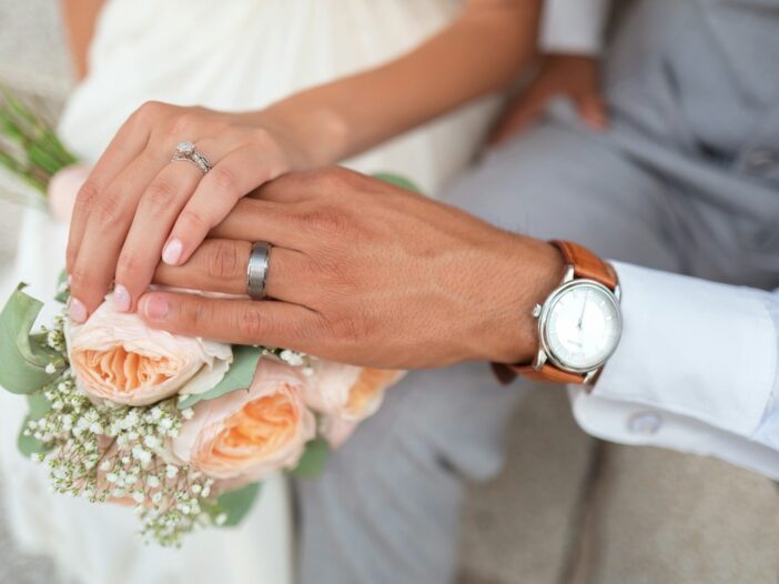 Bride and groom showing their wedding rings over a peach rose bouquet, illustrating short wedding Bible verses about love and marriage.