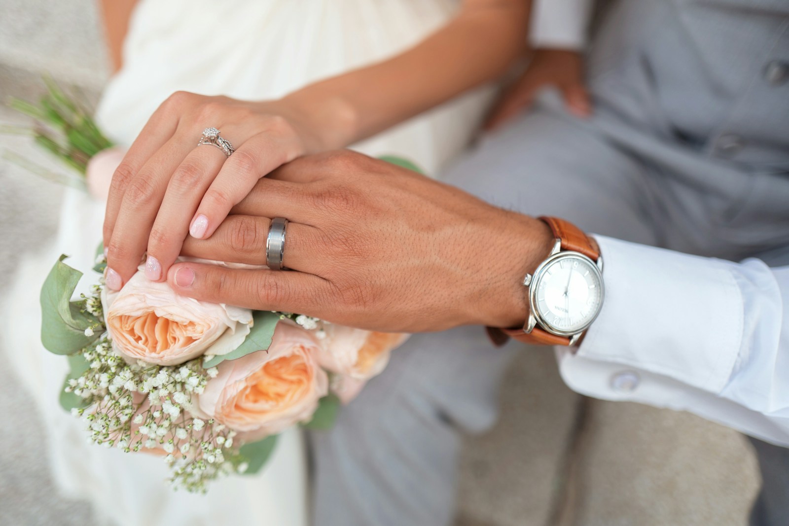Bride and groom showing their wedding rings over a peach rose bouquet, illustrating short wedding Bible verses about love and marriage.