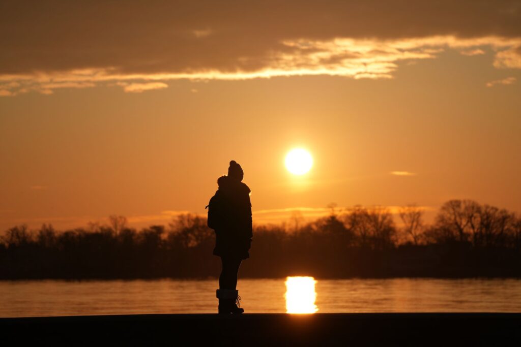 Silhouetted person standing by the water at sunrise for an article about the Philippians 4:13 meaning and strength through hardship.