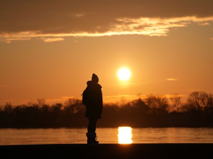 Silhouetted person standing by the water at sunrise for an article about the Philippians 4:13 meaning and strength through hardship.