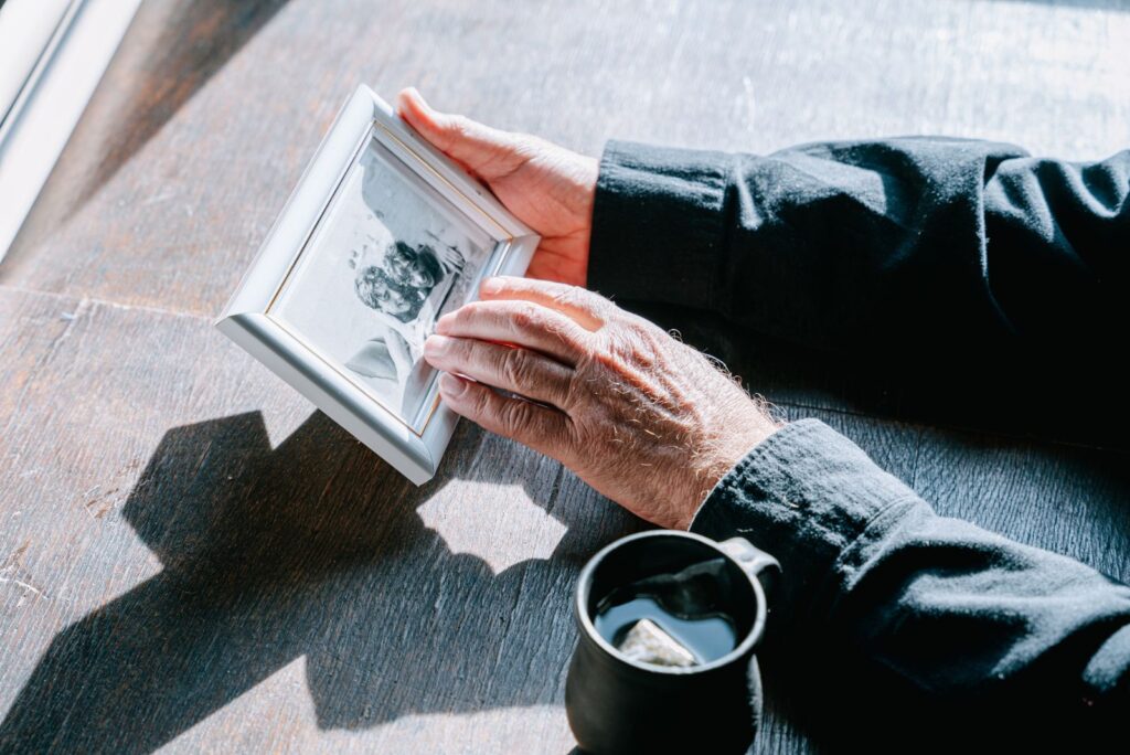 Person holding a framed photo of a loved one while grieving, for an article with Bible quotes about death of a loved one.