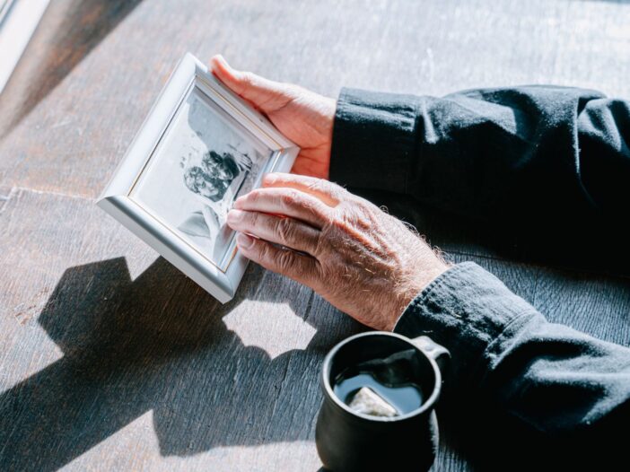 Person holding a framed photo of a loved one while grieving, for an article with Bible quotes about death of a loved one.