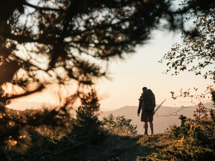 Hiker overlooking a mountain landscape at sunrise, symbolizing courage and trust in the meaning of Joshua 1:9.
