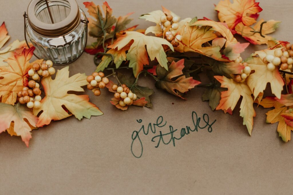 Thanksgiving wishes theme with “give thanks” handwritten among warm autumn leaves and seasonal decorations.