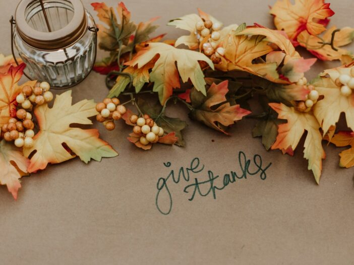 Thanksgiving wishes theme with “give thanks” handwritten among warm autumn leaves and seasonal decorations.
