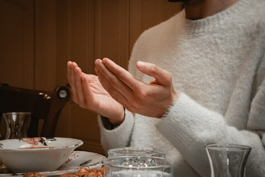 Person holding hands open in prayer before a Thanksgiving meal at the dinner table.