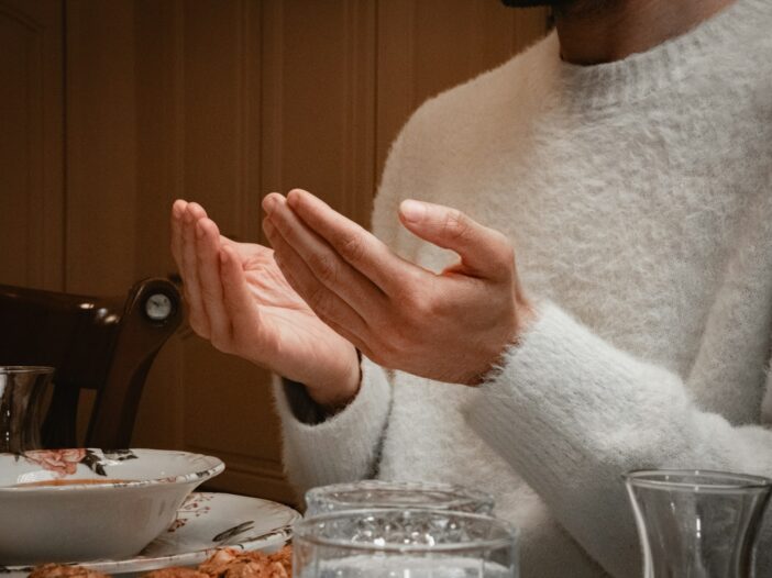 Person holding hands open in prayer before a Thanksgiving meal at the dinner table.