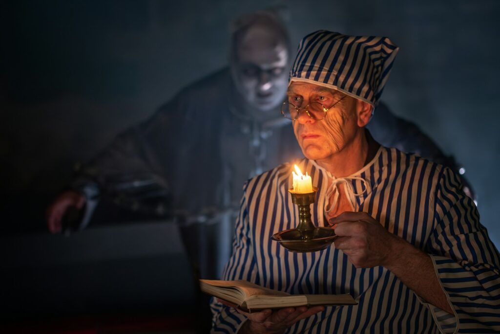 Ebenezer Scrooge holding a candle as a ghost appears behind him in A Christmas Carol.
