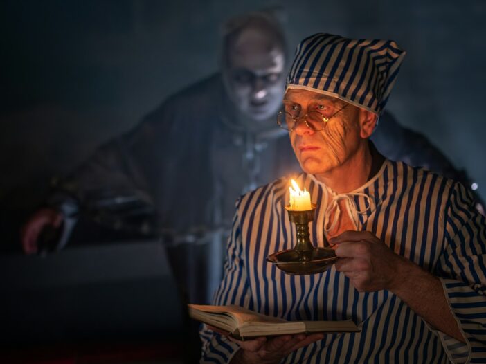 Ebenezer Scrooge holding a candle as a ghost appears behind him in A Christmas Carol.