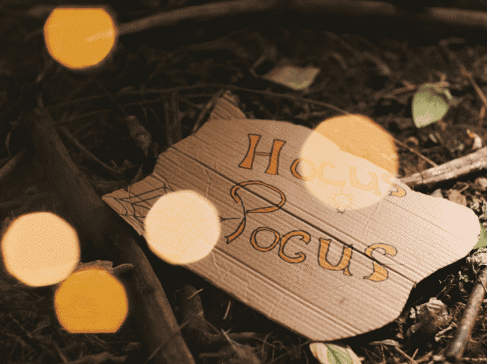 Handmade Hocus Pocus sign resting on the forest floor with warm Halloween lights