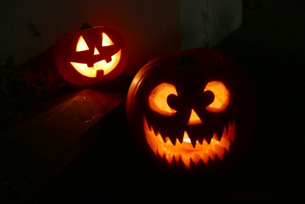 Two glowing jack-oโ-lanterns with playful carved faces on dark outdoor steps, illustrating funny and short Halloween quotes