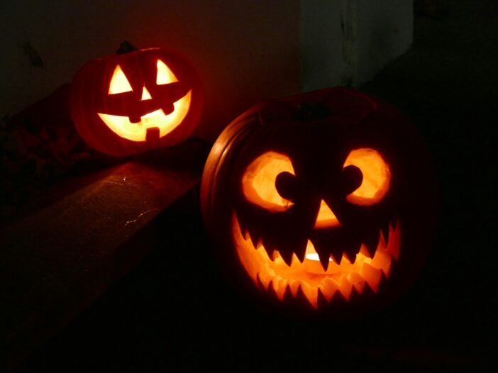 Two glowing jack-o’-lanterns with playful carved faces on dark outdoor steps, illustrating funny and short Halloween quotes
