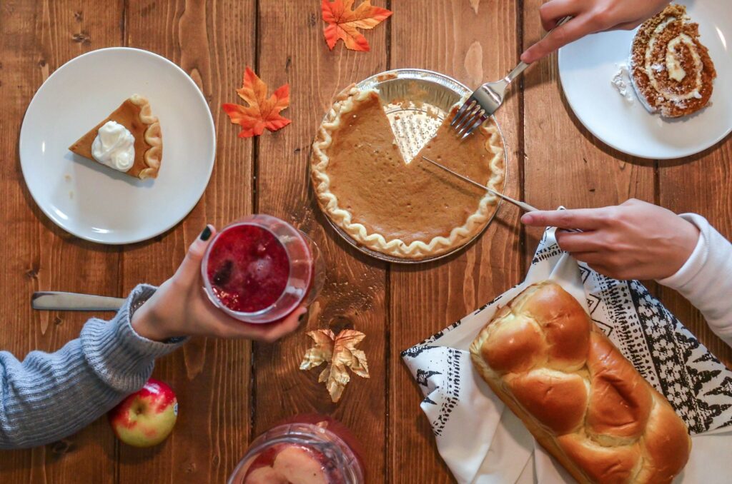 Family sharing pumpkin pie and food around a Thanksgiving table decorated with autumn leaves.