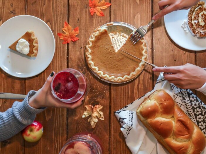 Family sharing pumpkin pie and food around a Thanksgiving table decorated with autumn leaves.