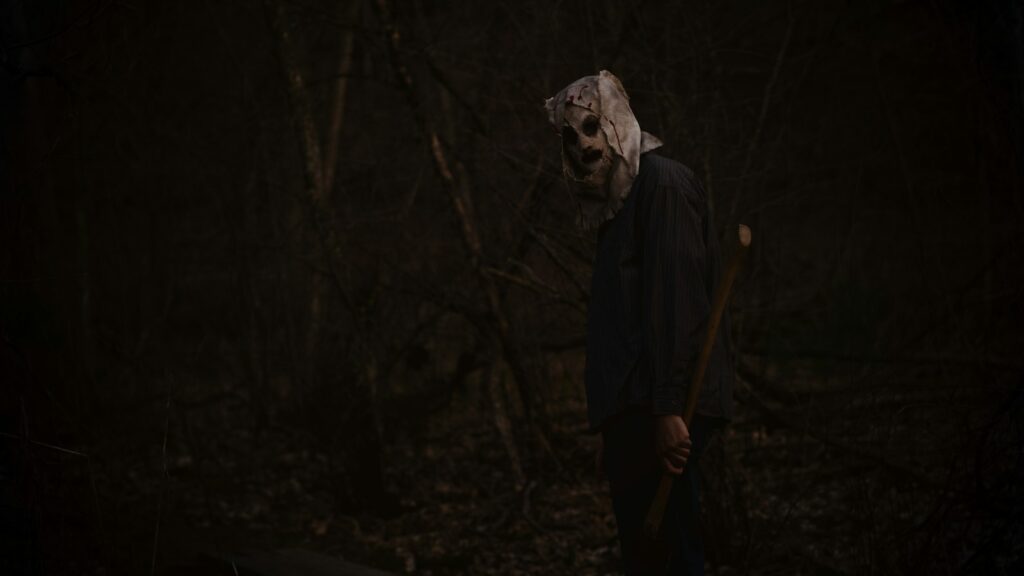 Masked horror figure standing in a dark forest to illustrate a collection of Halloween movie quotes.