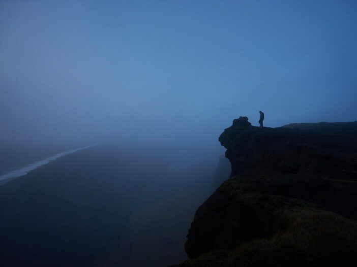 Lone figure standing on a foggy cliff to illustrate the Nietzsche abyss quote about gazing into the abyss