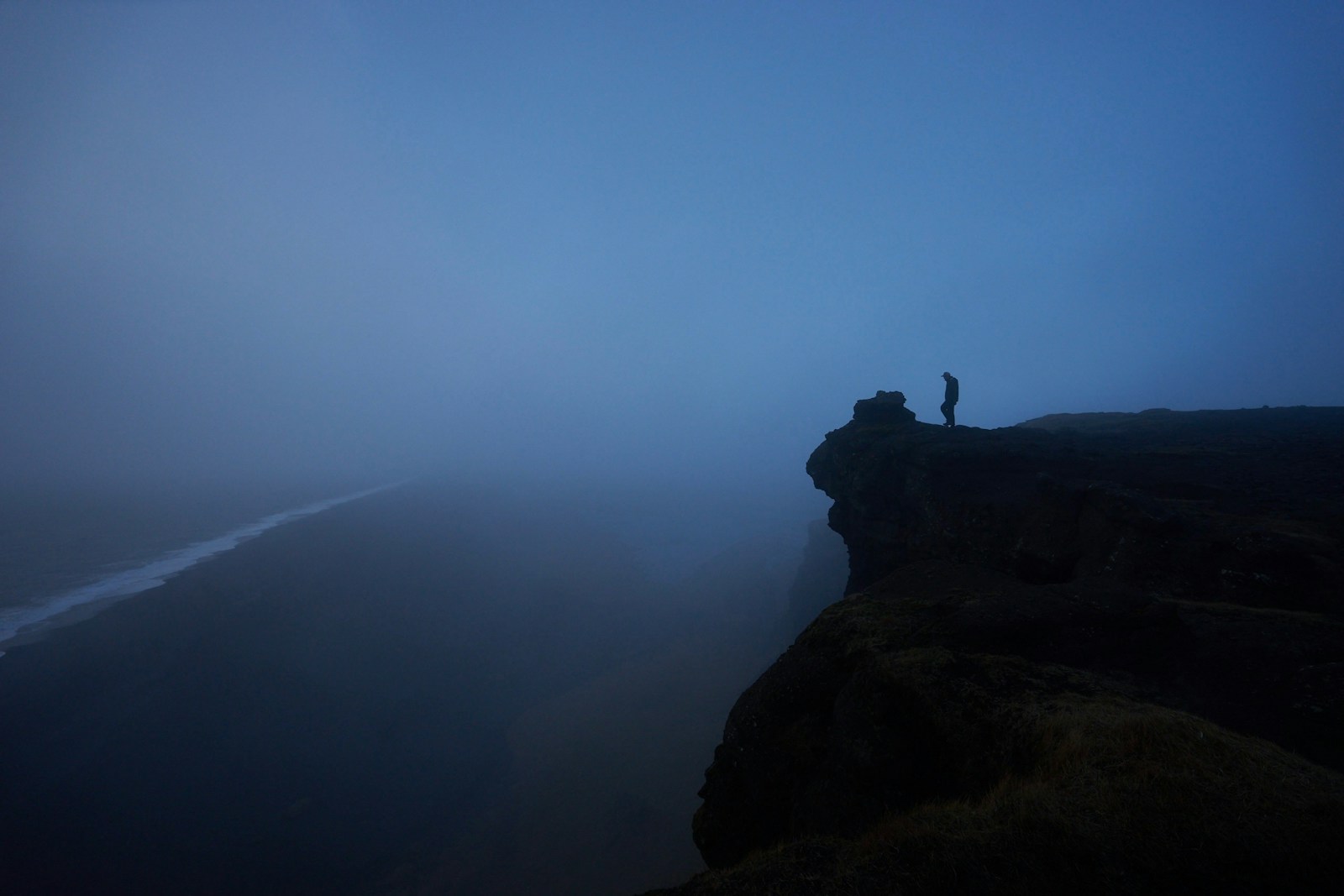 Lone figure standing on a foggy cliff to illustrate the Nietzsche abyss quote about gazing into the abyss