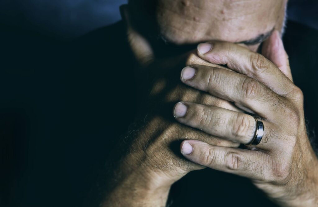 Close-up of an elderly man covering his face, expressing grief and contemplation.