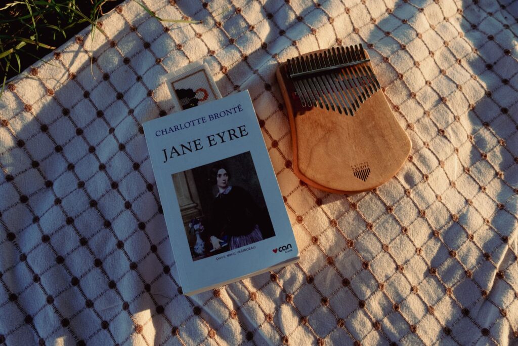 A vintage book 'Jane Eyre' beside a kalimba on a warm-patterned blanket.