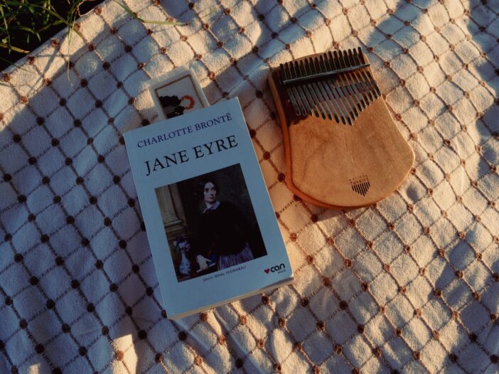 A vintage book 'Jane Eyre' beside a kalimba on a warm-patterned blanket.