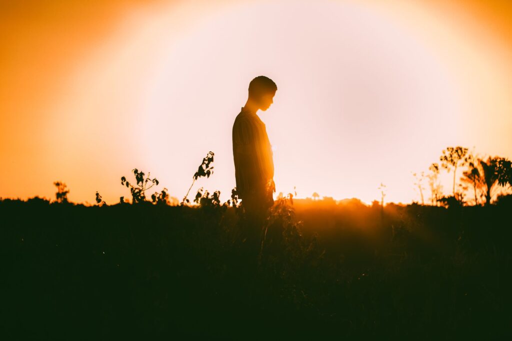 A captivating silhouette of a person standing in a field against a vibrant sunset backdrop.