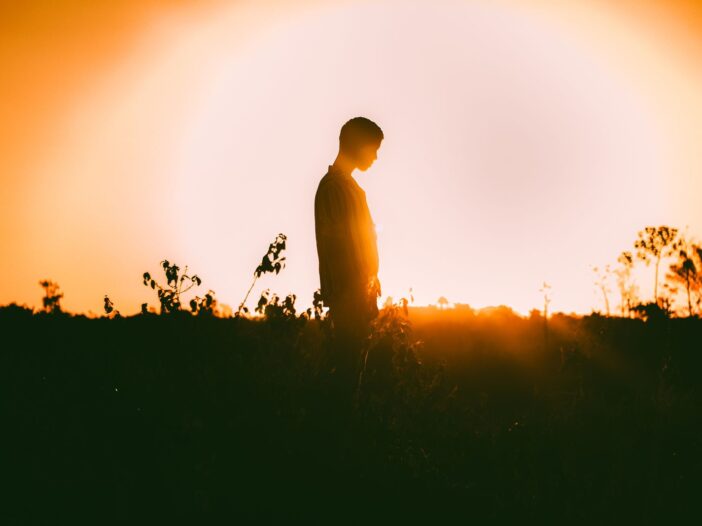 A captivating silhouette of a person standing in a field against a vibrant sunset backdrop.