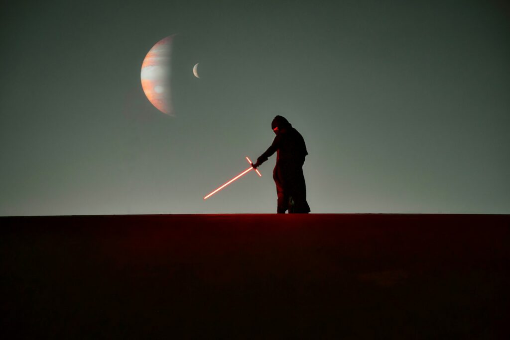 Silhouetted figure holding a red crossguard lightsaber beneath distant planets in a Star Wars-inspired landscape