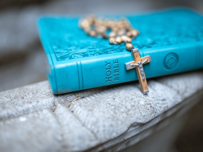 A teal Holy Bible with a rosary resting on a marble surface, symbolizing faith and devotion.