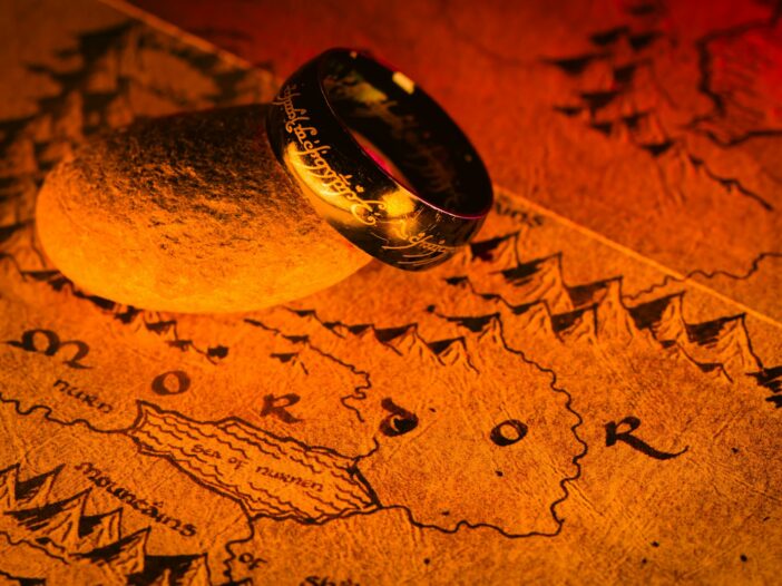 The One Ring resting on a stone above Mordor on a warmly lit Middle-earth map, illustrating lord of the rings quotes.
