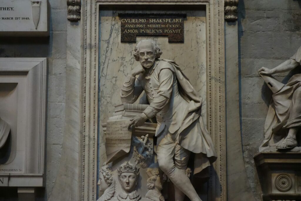 Marble statue of William Shakespeare leaning on books in a stone wall niche