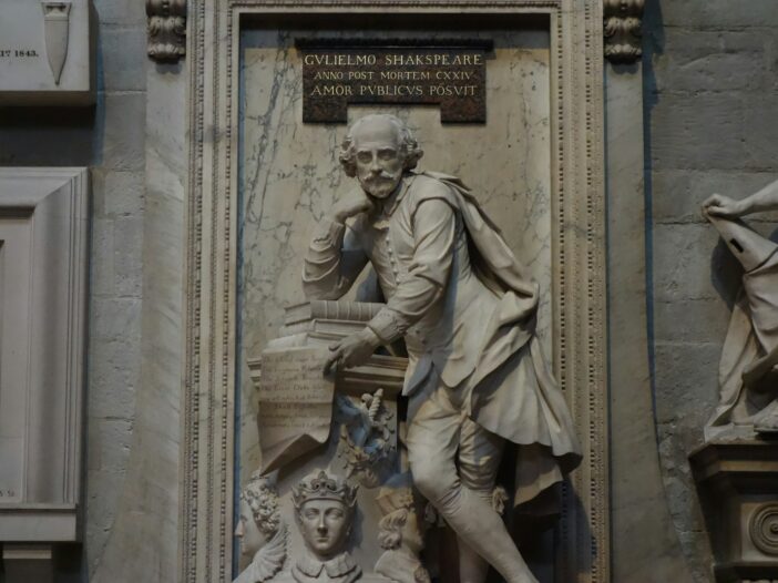 Marble statue of William Shakespeare leaning on books in a stone wall niche