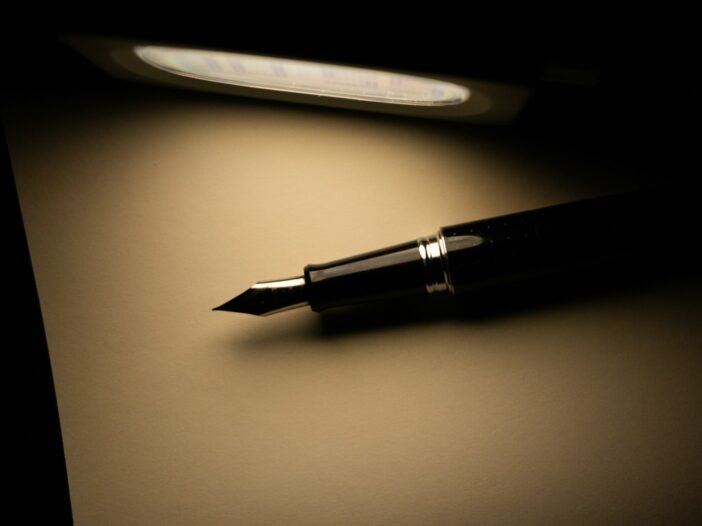 a fountain pen sitting on top of a dark table next to a light