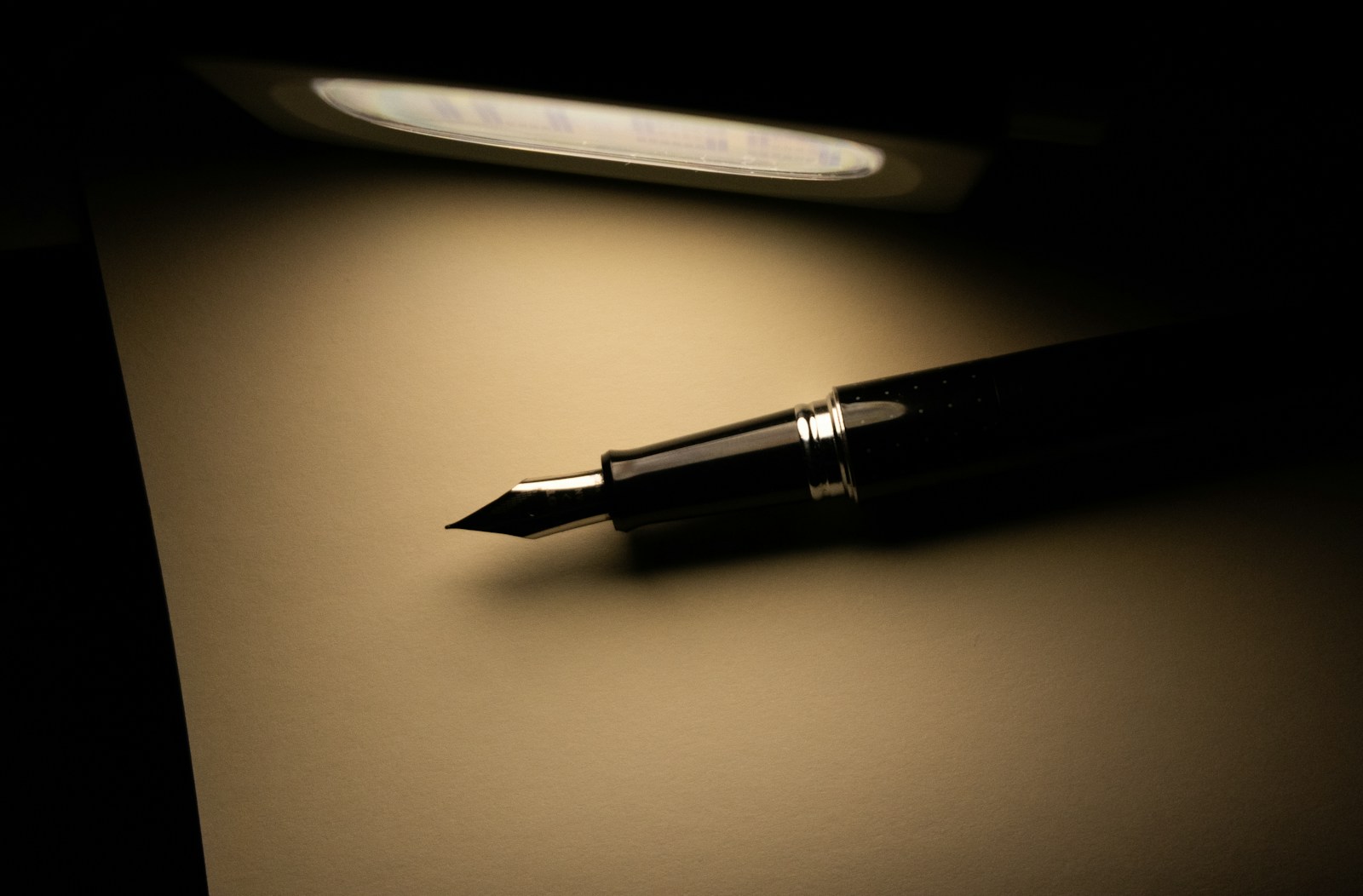 a fountain pen sitting on top of a dark table next to a light