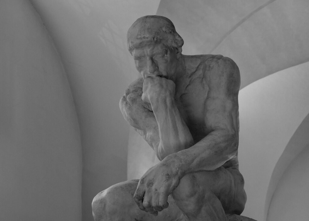 Black-and-white photograph of a seated sculpture resting its chin on one hand in contemplation, illustrating greatest philosophers of all time