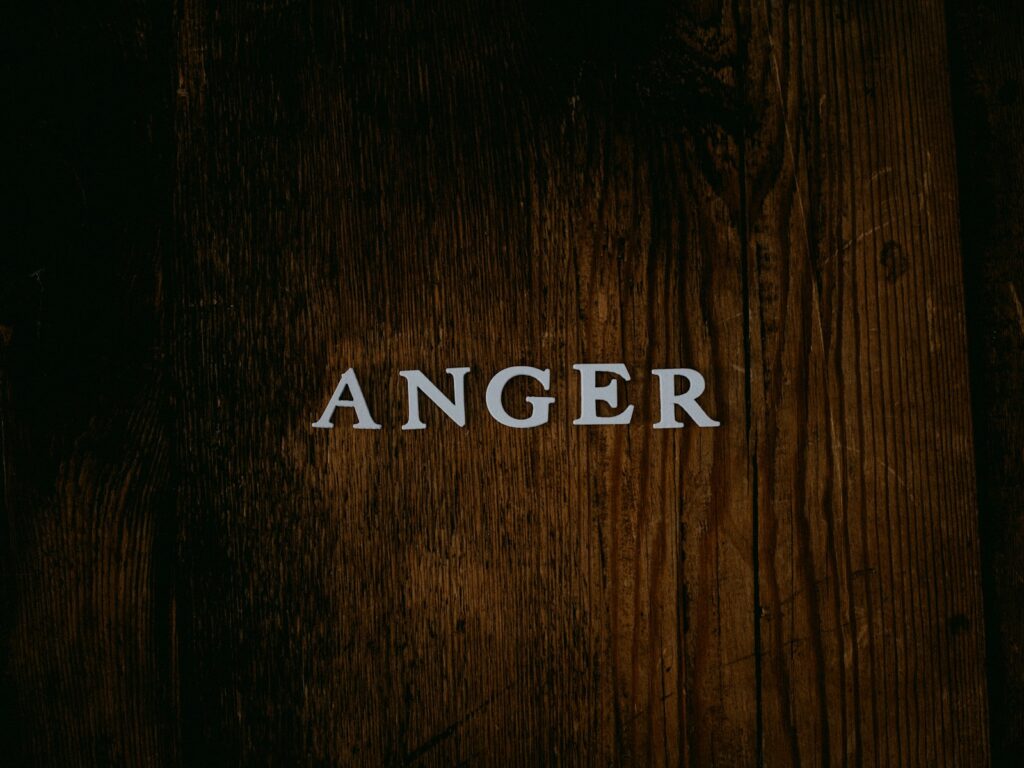 The word anger against a dark wooden background, representing bible quotes about anger